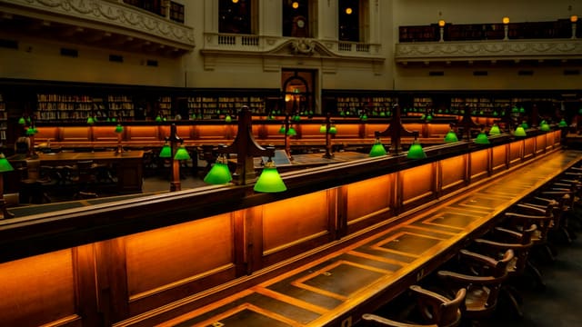 Grand library interior with long wooden tables and green lamps