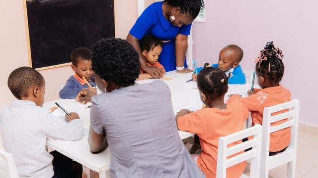 Teacher guiding children drawing at a table