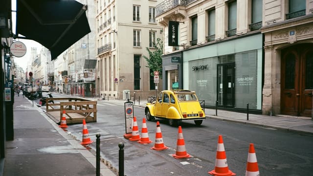 Yellow car driving past traffic cones on a city street