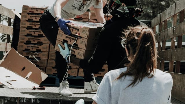 Three people wearing masks loading cardboard boxes of strawberries onto a truck bed