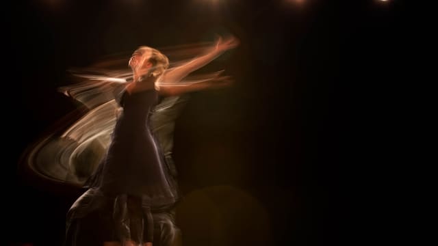 A dancer in a dark dress performing with long exposure motion blur