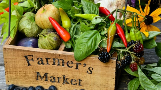 A wooden crate labeled Farmer's Market filled with fresh tomatillos, chili peppers, and blackberries