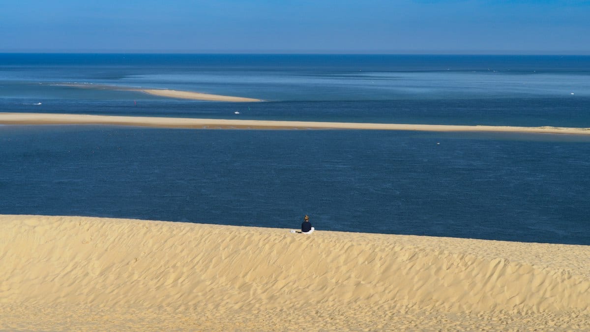 Silhouette d'une personne au sommet d'une dune de sable face à l'océan