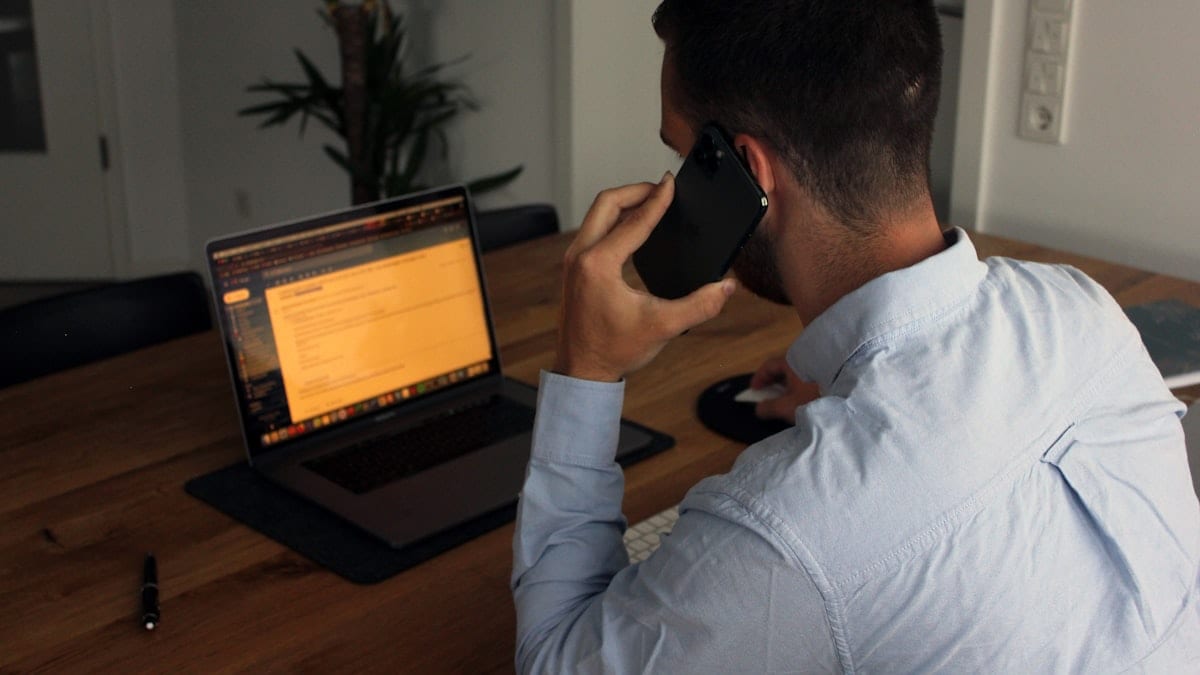 man in blue dress shirt holding black smartphone