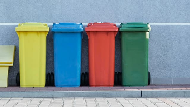 Quatre bacs à déchets de couleurs différentes alignés contre un mur