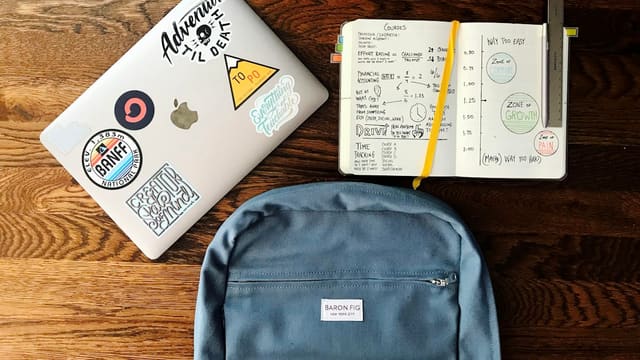 flat lay photography of blue backpack beside book and silver MacBook