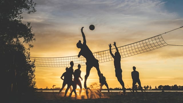 Silhouettes jouant au beach-volley au coucher du soleil