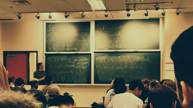 student sitting on chairs in front of chalkboard