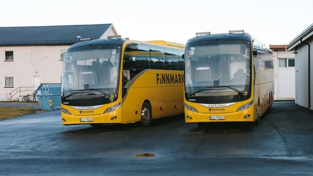 Two yellow tour buses parked outside buildings